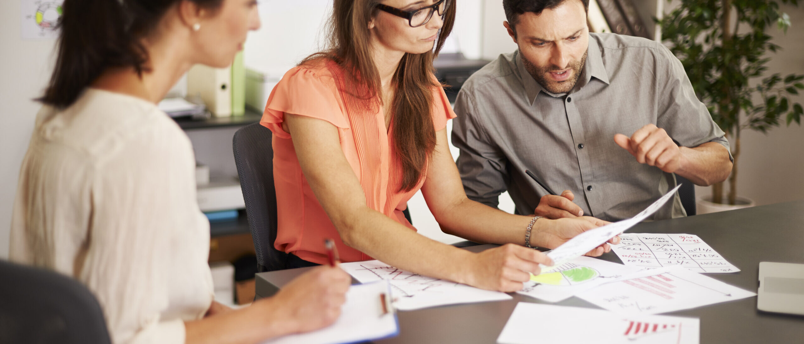 Three professionals reviewing charts and data in an office during a workforce planning meeting