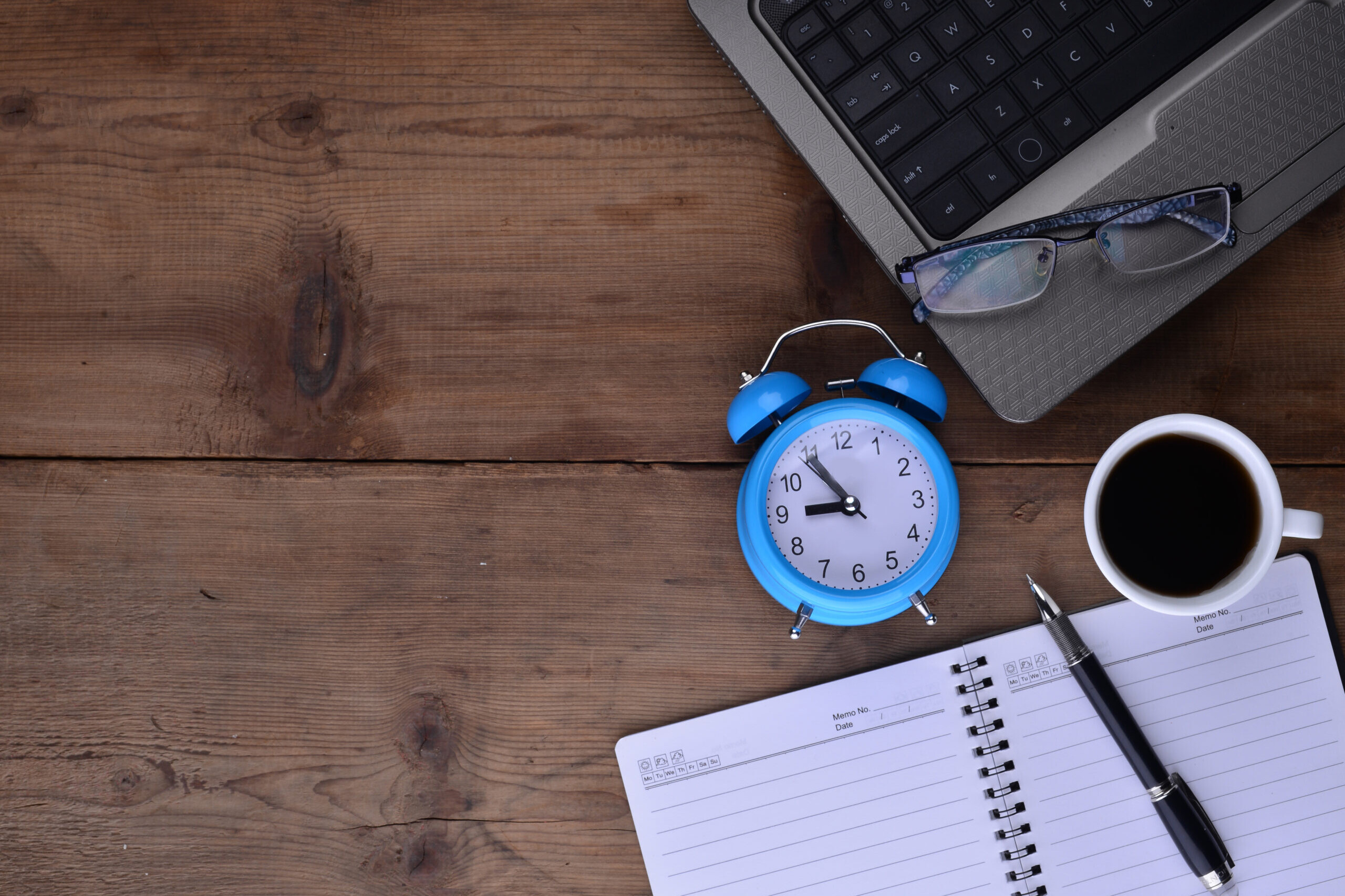 Desk with notebook, clock, laptop, and coffee representing time off policy planning and PTO tracking